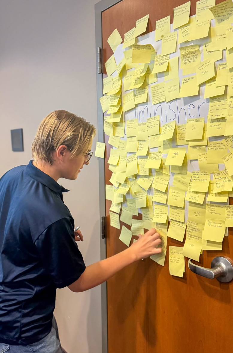A student adding a sticky note to a wall of ideas
